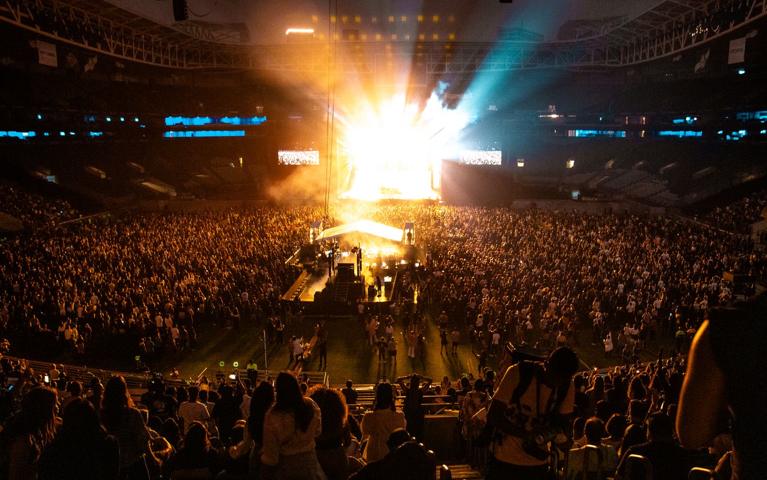 A packed arena at night with the stage lit in front of the crowd