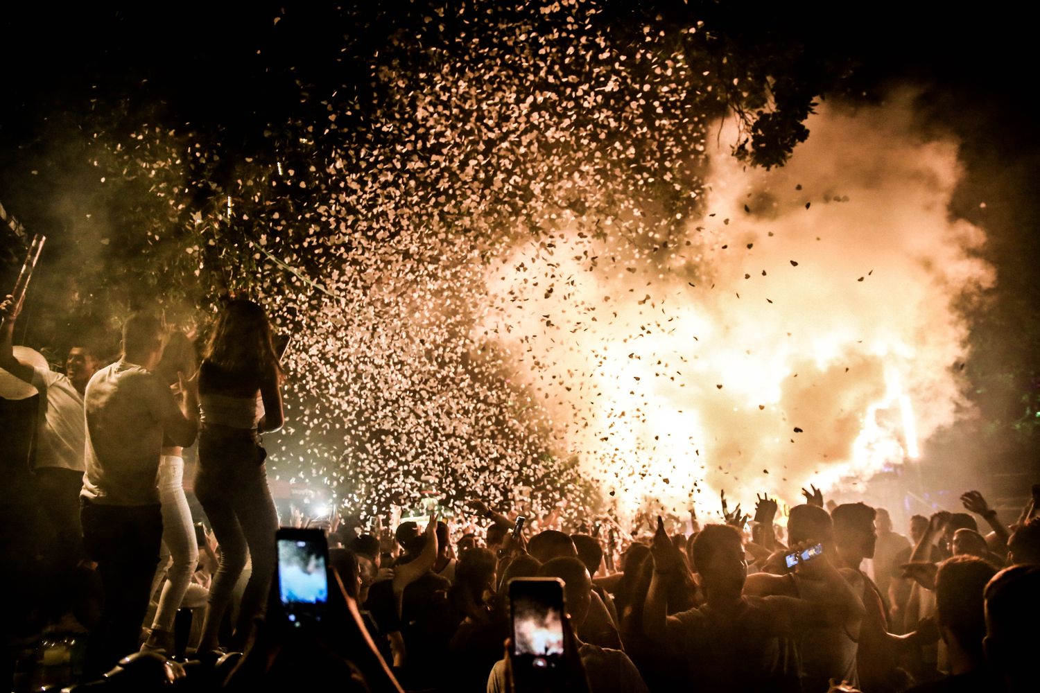 A night crowd dancing under a burst of confetti and stage light