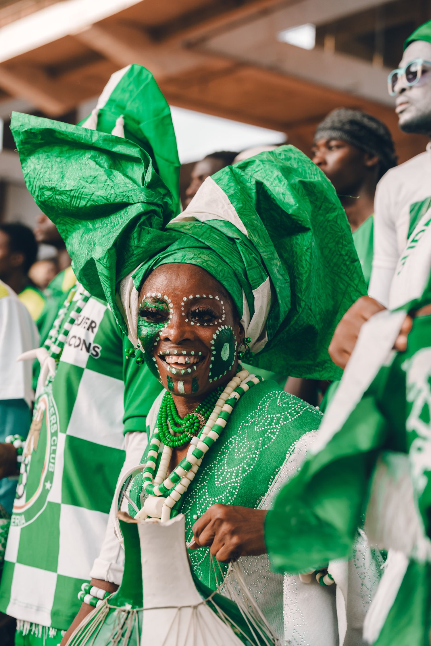 A woman in a green and white gele with traditional face paint at a Nigerian celebration