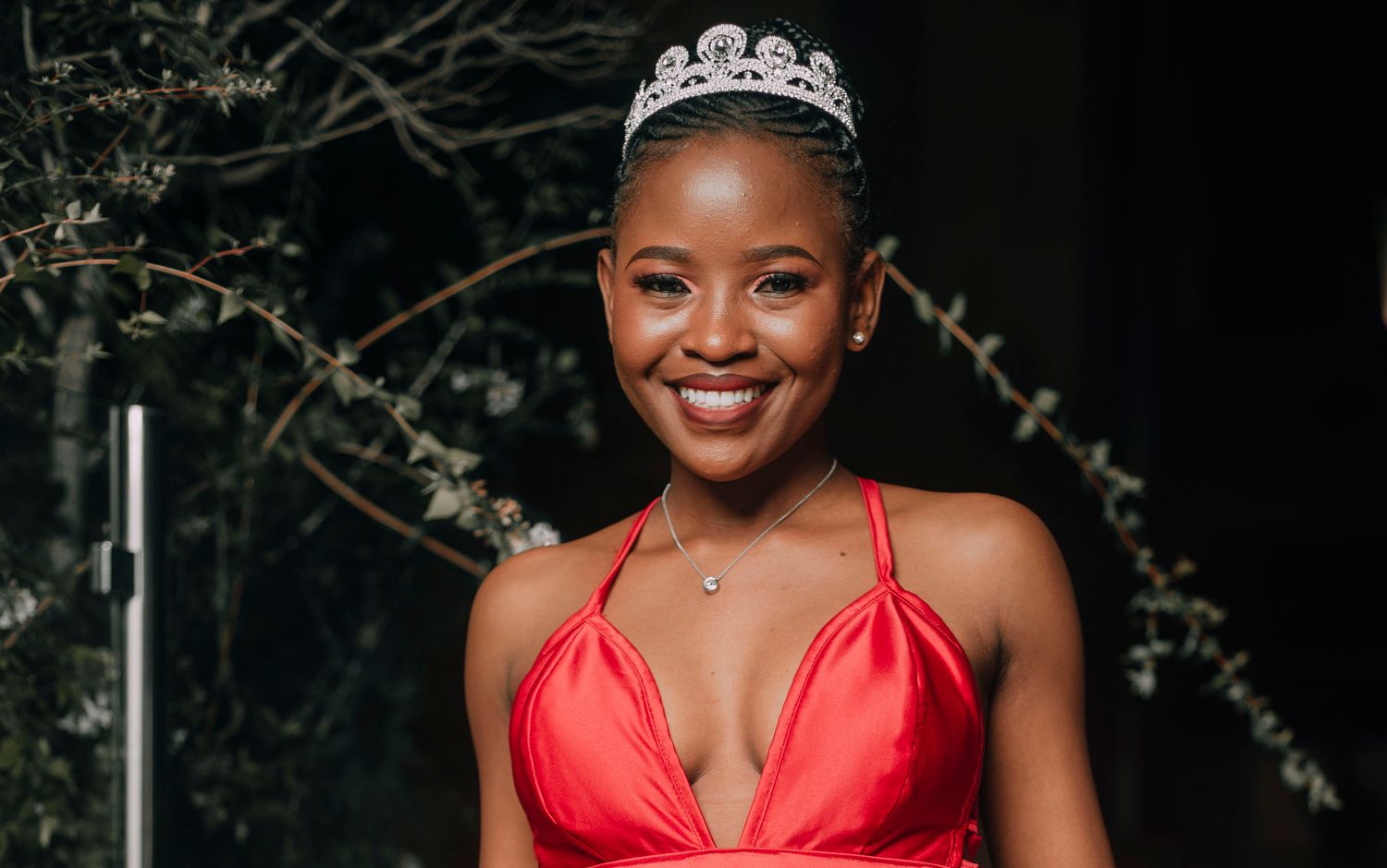 A crowned pageant contestant in a red evening gown at an awards night