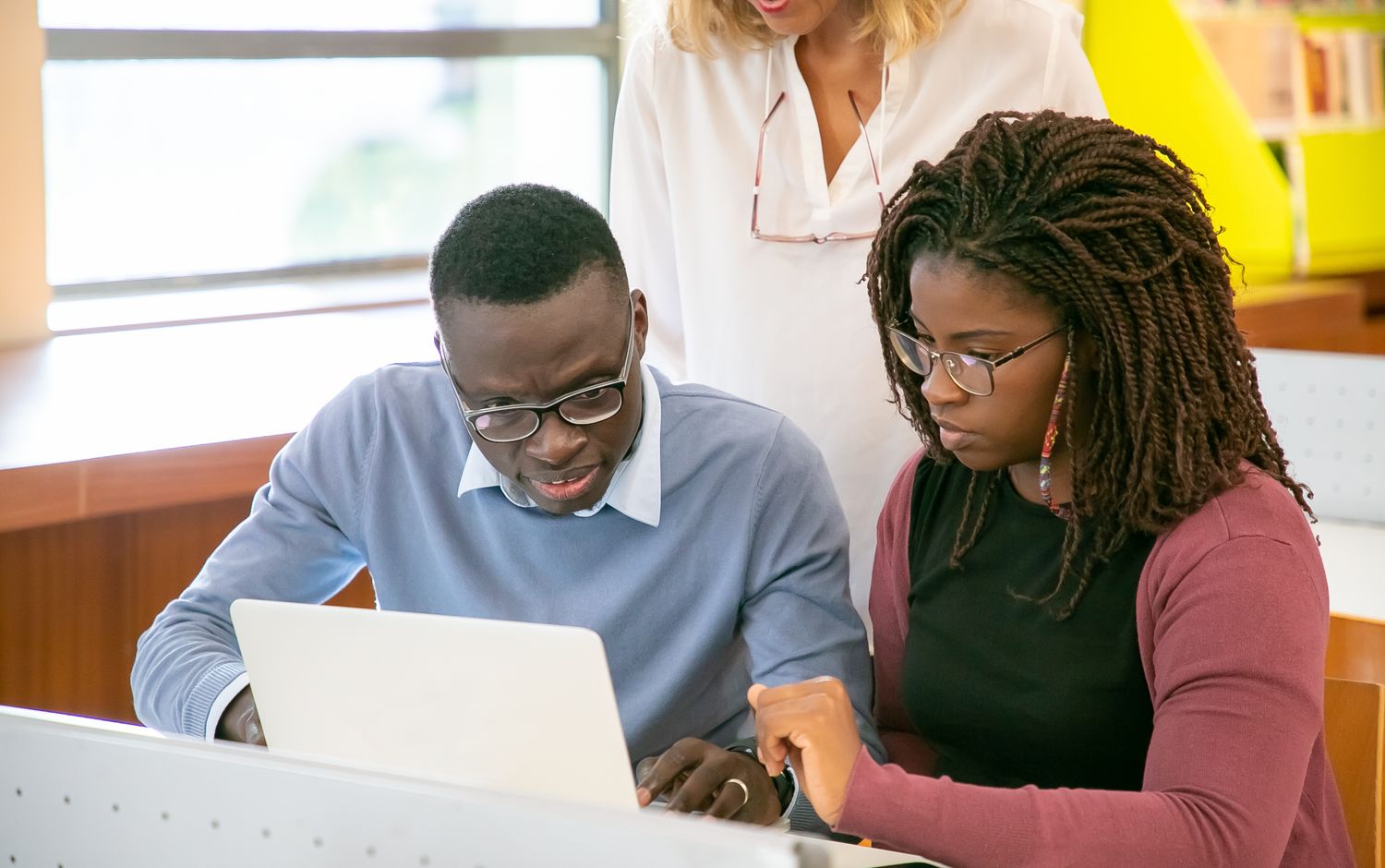 Young students learning at a laptop with a trainer beside them